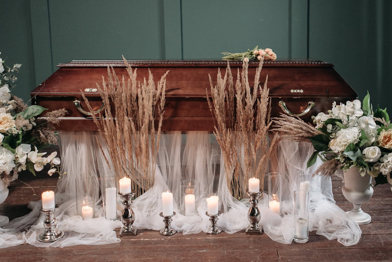 An elegant funeral setting featuring a coffin surrounded by flowers and lit candles, creating a serene atmosphere.